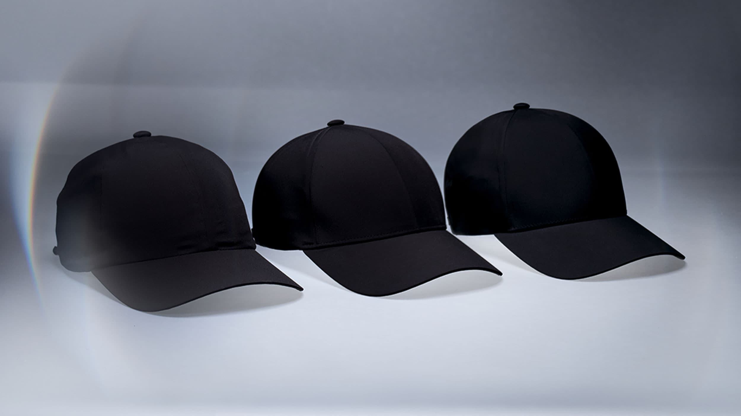 Three black sport caps aligned in a row against a light gradient background.
